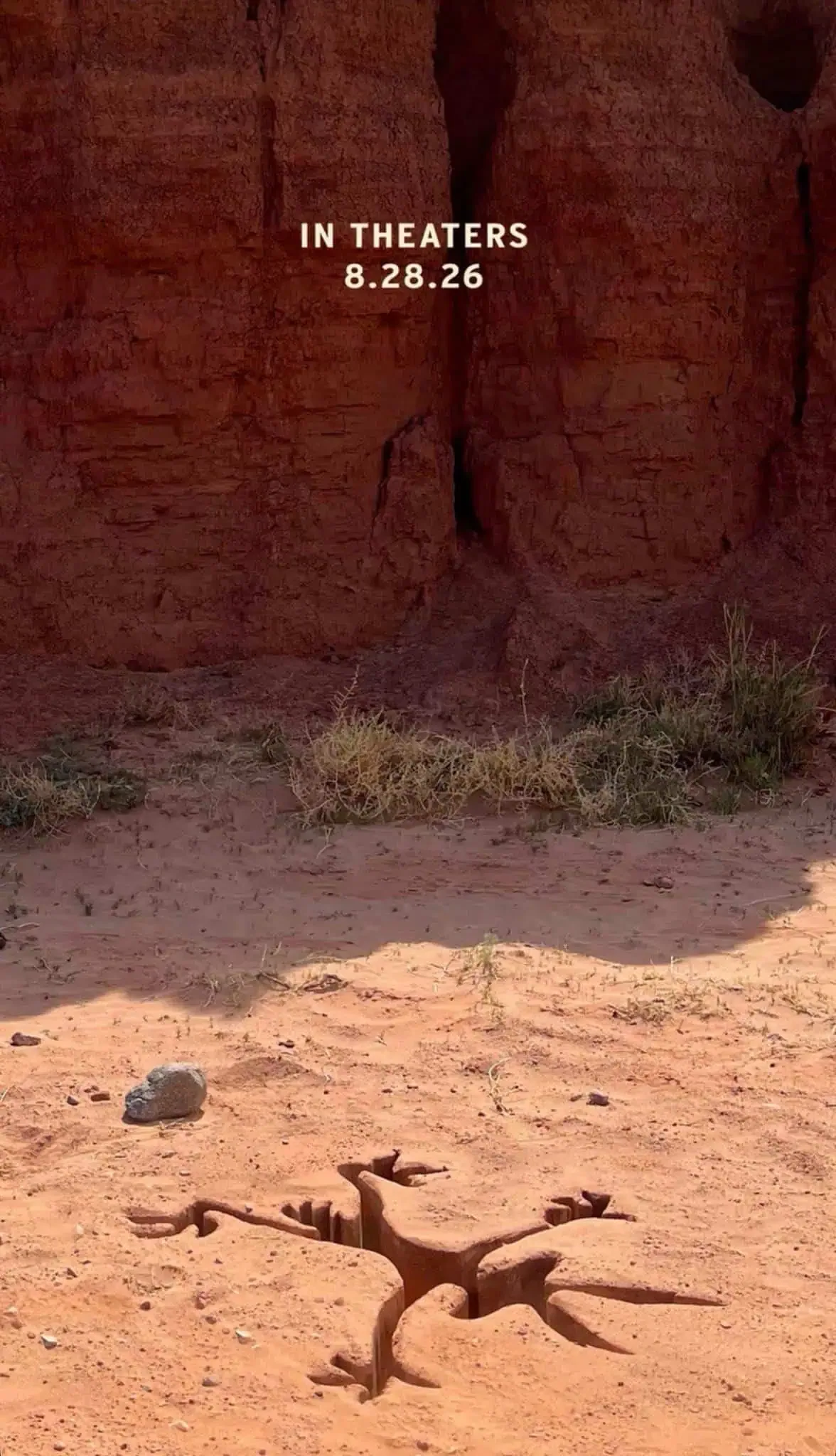 A Wile E. Coyote-shaped imprint pressed into red desert sand beneath a canyon wall.
