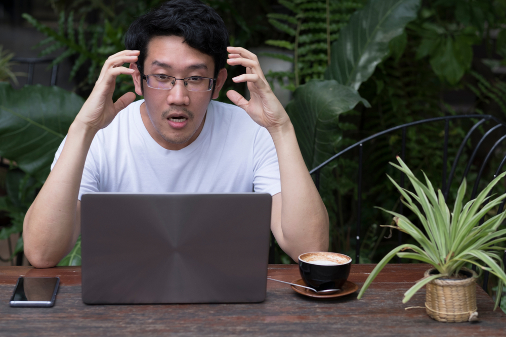 A surprised man behind a laptop staring at the screen with a shocked or frustrated expression.