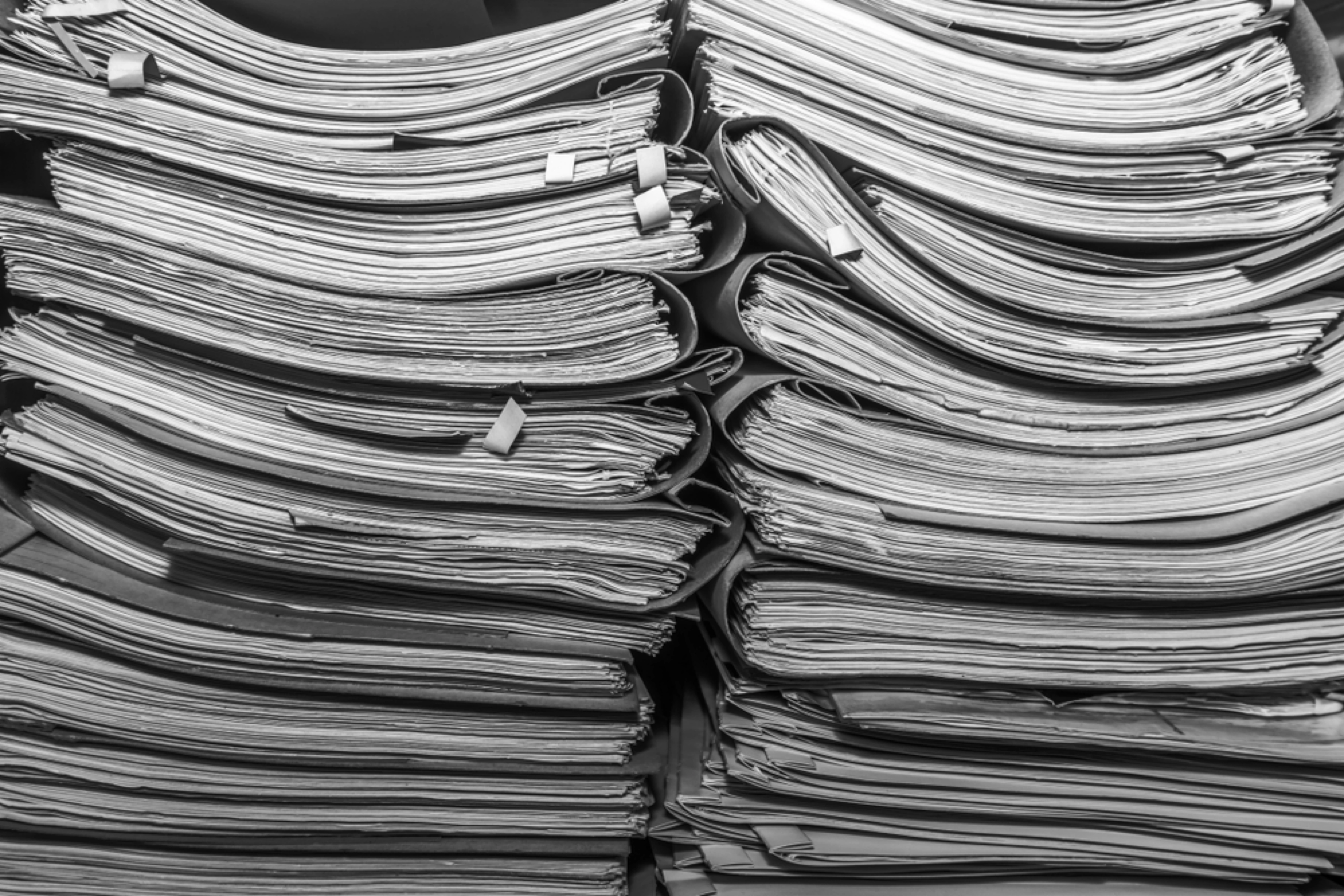 Rows of shelves in an archive room packed with stacked paper documents and files.
