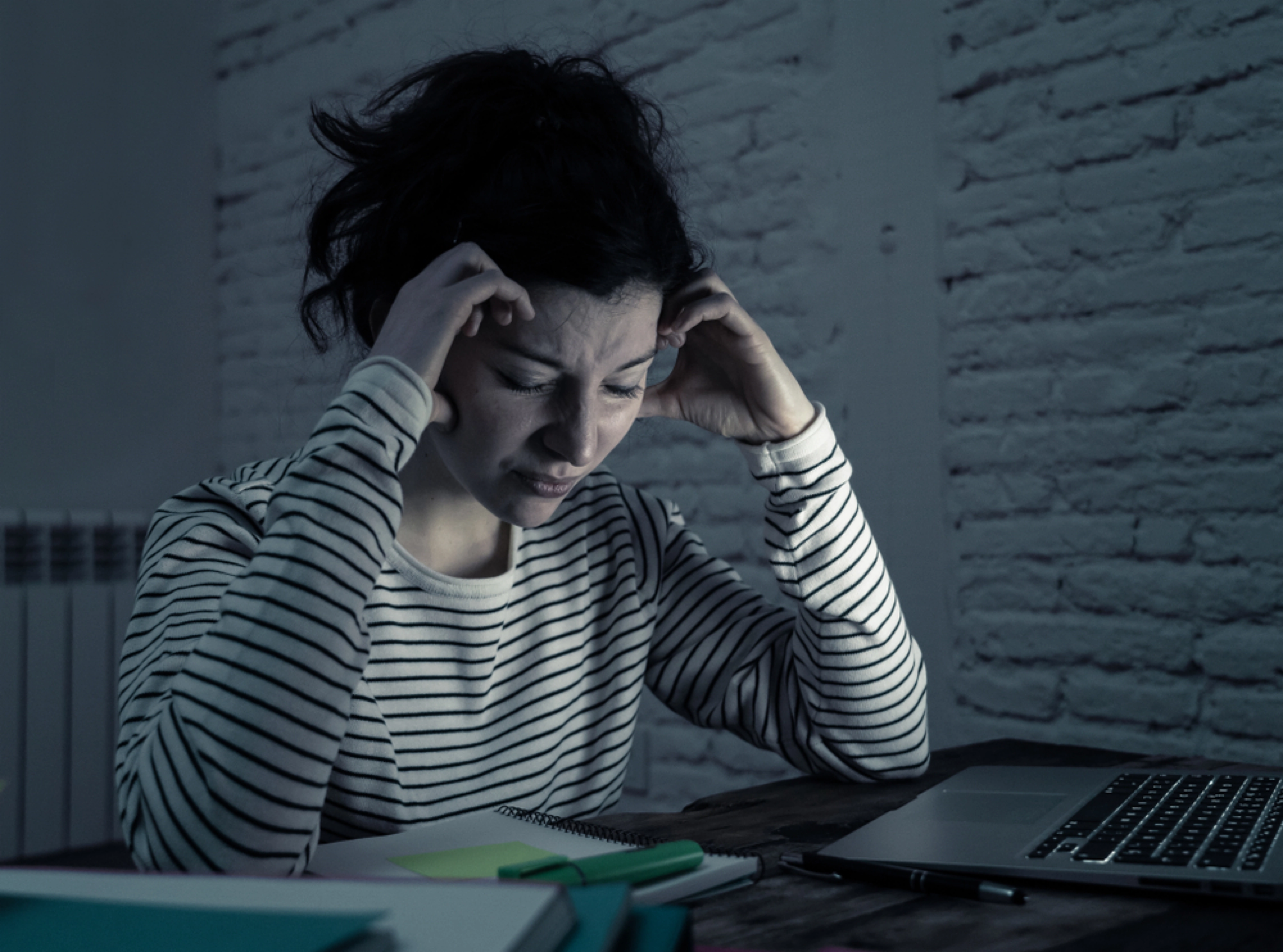 A woman at a laptop late at night, focused on a glowing screen in a dimly lit room.